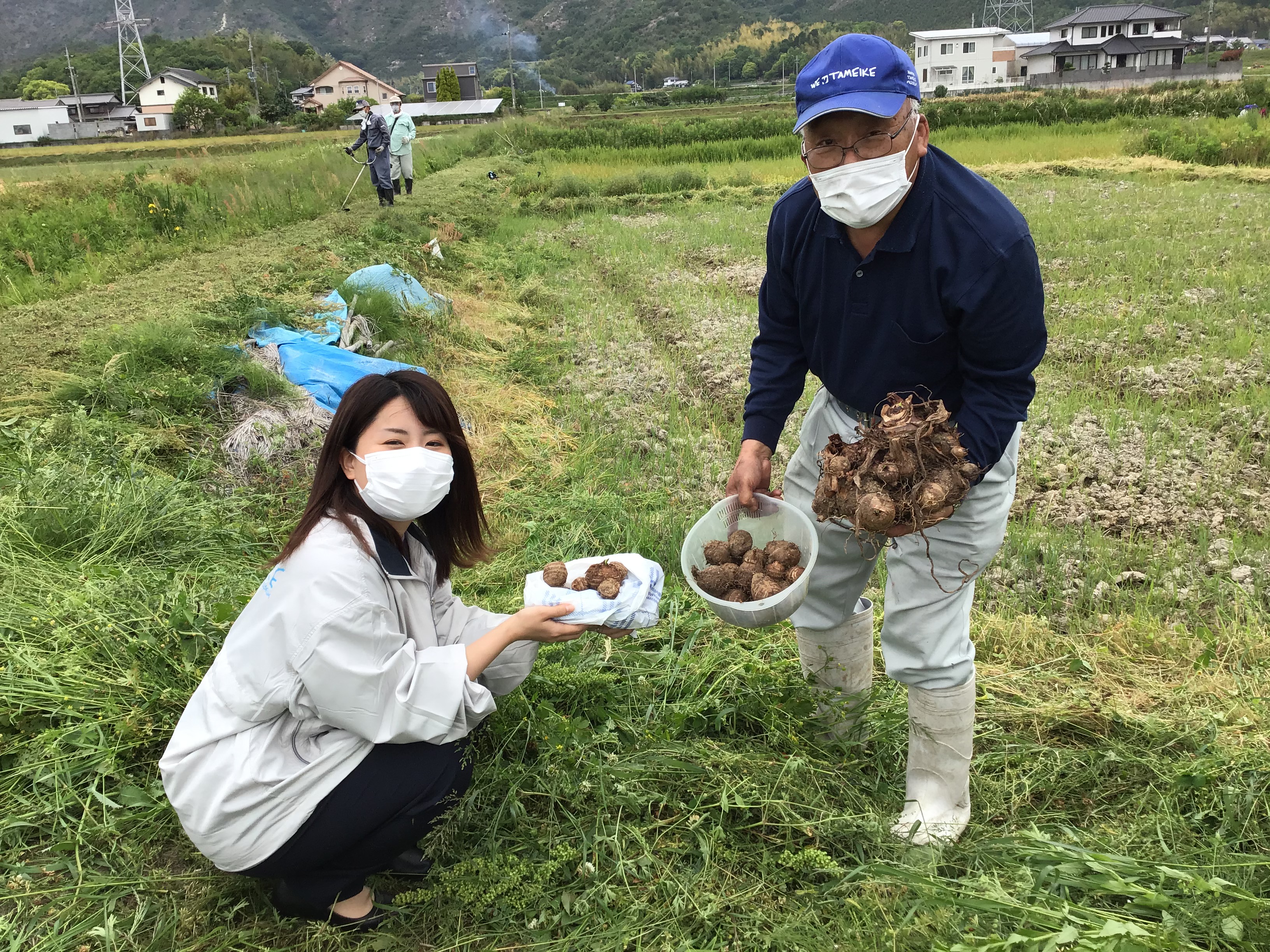 現場確認に訪れた東播磨県民局の福田さん(左)に里芋植付けで種芋の説明をする高砂市ため池協議会の黒田会長(右)